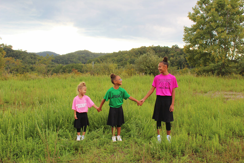 Three young girls wearing black skirted leggings holding hands in a field 