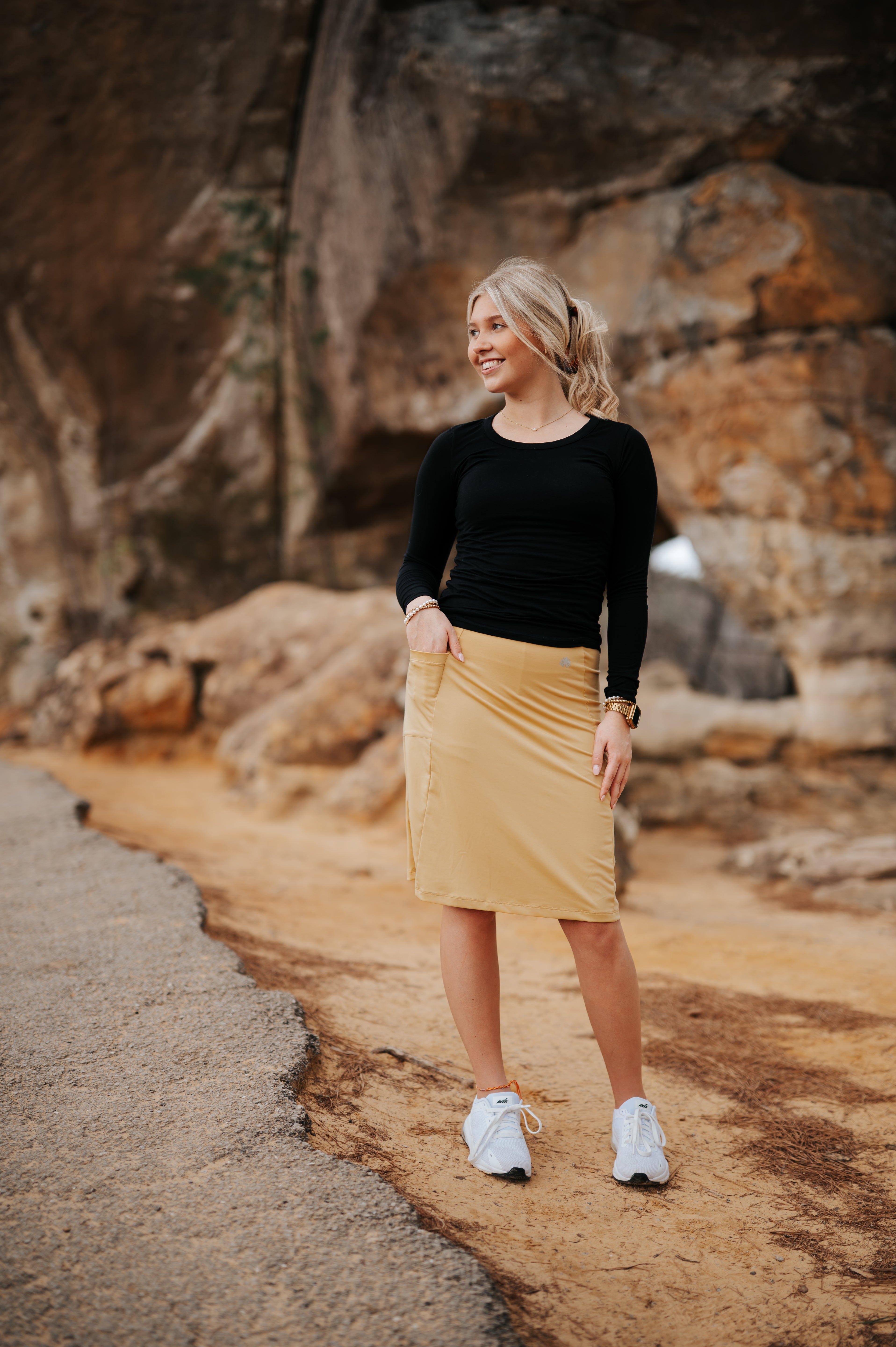 Woman in Snoga Athletics modest activewear skirt and black top standing outdoors on rocky path
