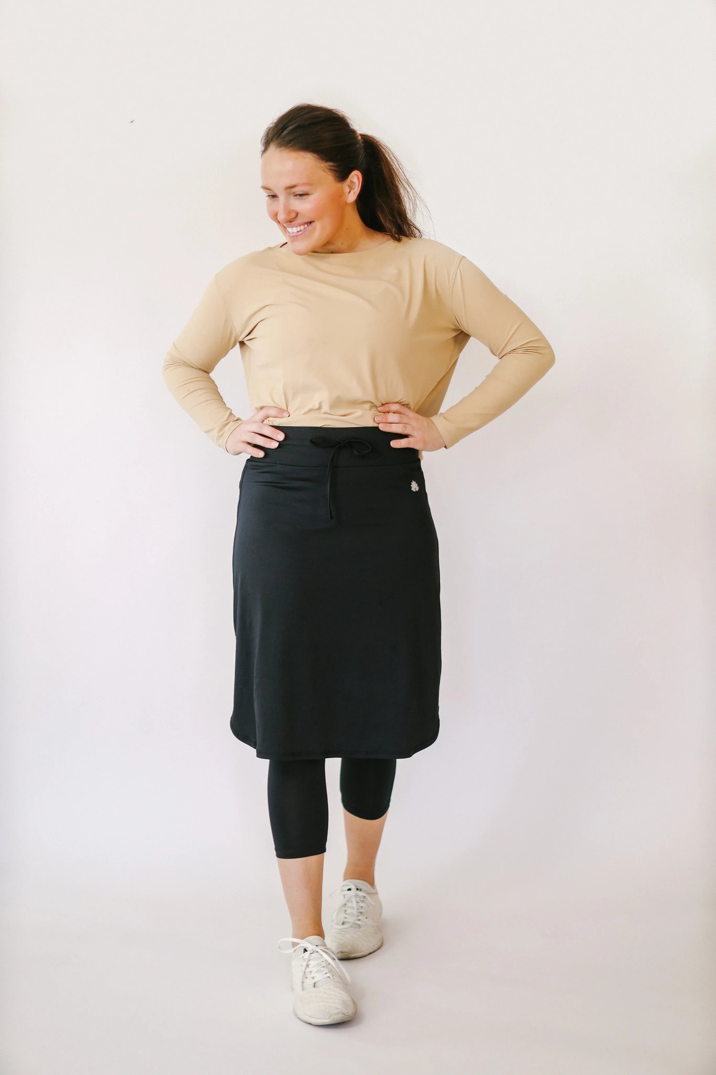 Woman wearing Snoga Athletics black drawstring capri skirt with leggings, long sleeve top, and sneakers.