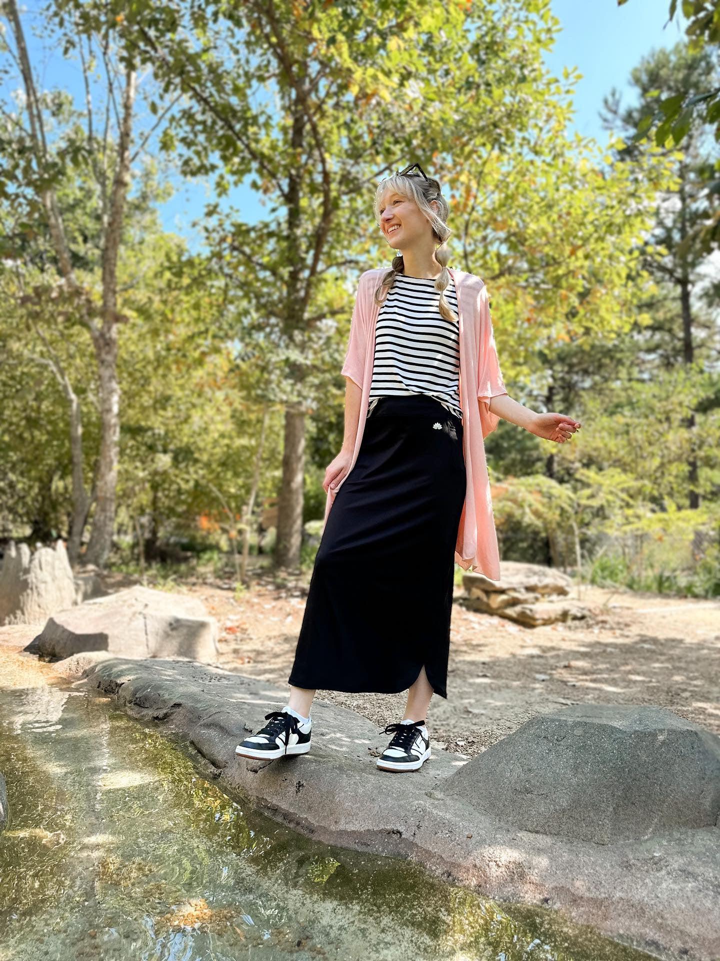Woman outdoors wearing Snoga Athletics black maxi active skirt with pockets, striped top, and sneakers
