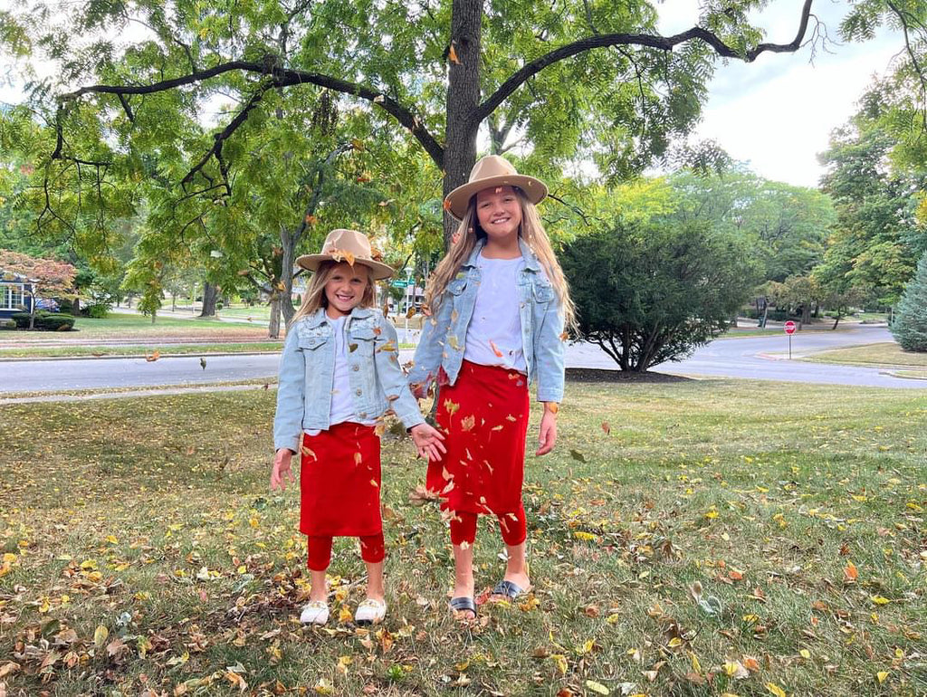 Two young girls wearing matching red skirted leggings and denim jackets
