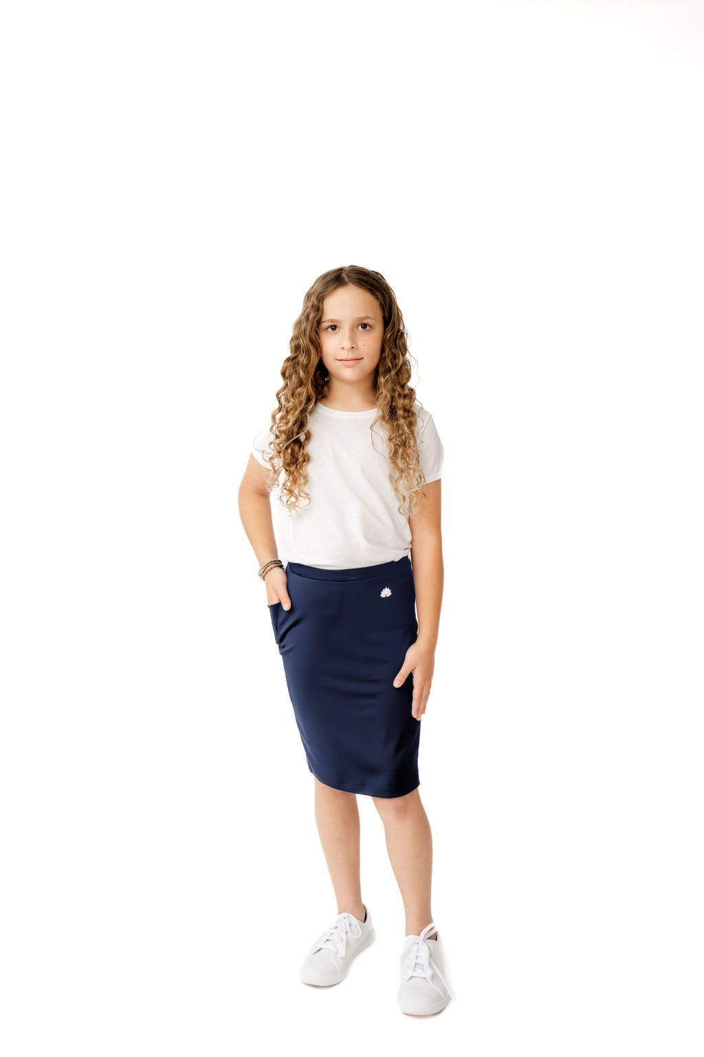 Young girl in white shirt and navy Snoga Athletics modest skirt with logo, white sneakers