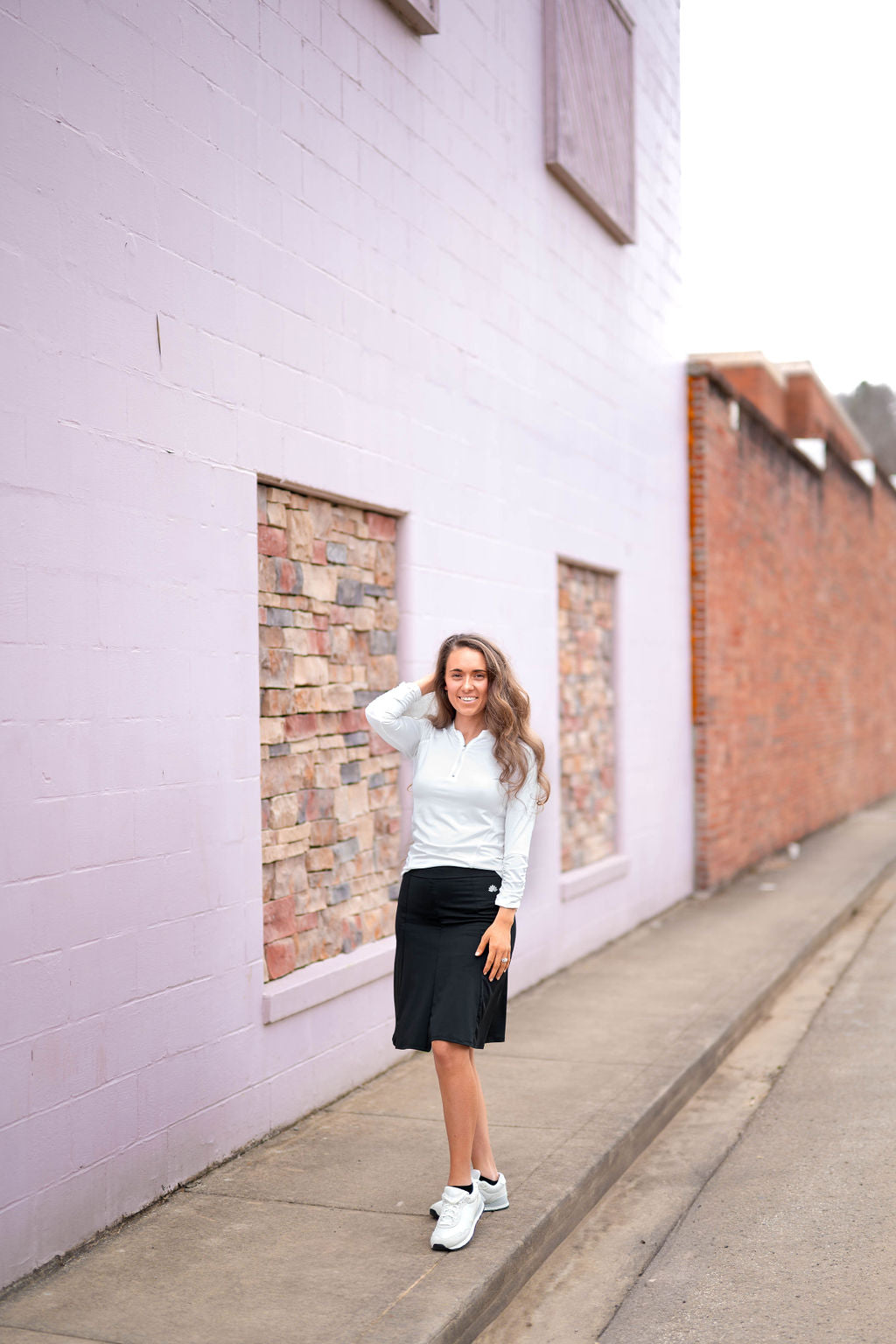 Woman wearing Snoga Athletics black modest skirt and white long sleeve top, standing on sidewalk