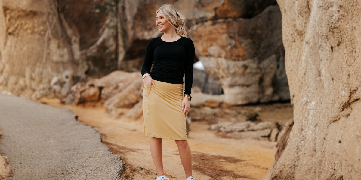 Woman wearing Snoga Athletics modest tan skirt and black top in natural rocky setting