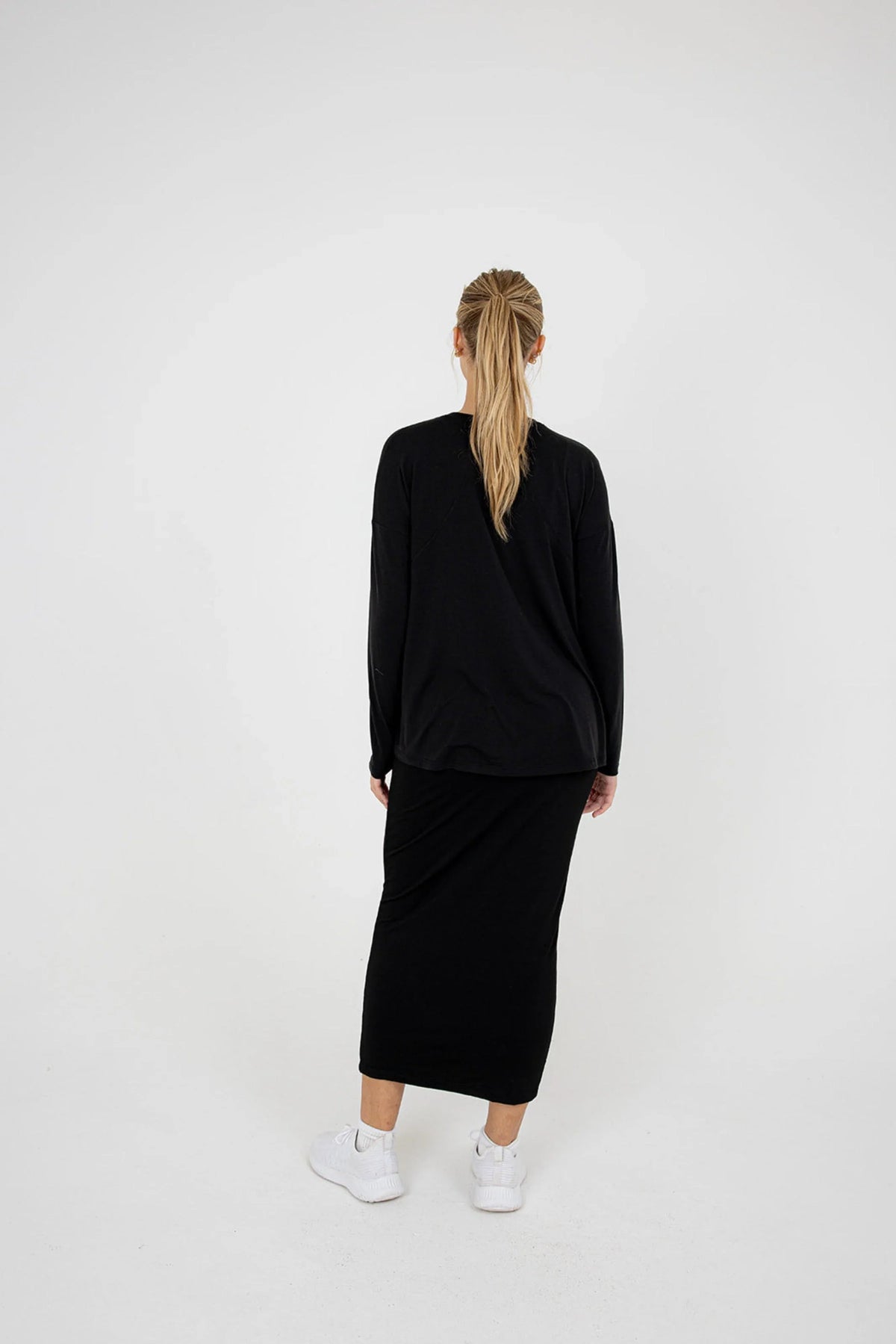 Woman in black Snoga Athletics t-shirt skirt set, back view, styled with white sneakers