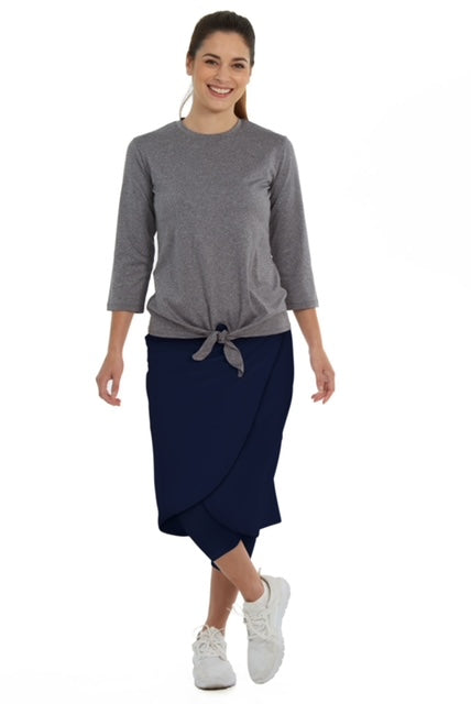 Woman wearing Snoga Athletics navy faux wrap skirt with leggings, gray top, and white sneakers